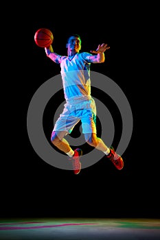 Athlete man basketball player passing ball in mid-air in action against black studio background in mixed neon light.