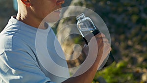 Athlete man drinking bottle water at ocean cliff closeup. Fit guy opening jug