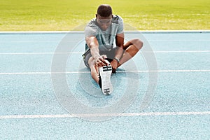 Athlete man, sitting and track for stretching legs to start training, exercise or running for fitness outdoor. African
