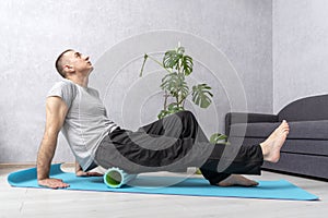 Athlete man stretches using foam roller at home. Man doing self-massage of the gluteal muscles with fascia roll