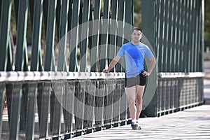 Athlete man stretching legs warming up calf muscles before running workout leaning on railing city urban park