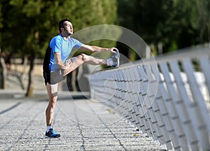 Athlete man stretching legs warming up calf muscles before running workout leaning on railing city urban park