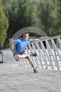 Athlete man stretching legs warming up muscles before running workout leaning on railing city urban park