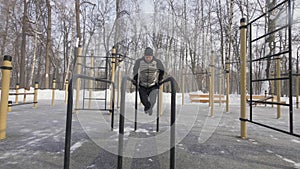 Athlete man training push ups exercise on bar on winter sport ground