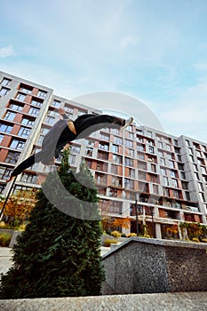 Athlete man, young guy jumping high, flips of wall in public park among high-rise buildings over sky view in action. Eye