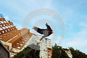 Athlete man, young guy jumping high, making back-flip over city, high-rise buildings and sky view in public park. Eye