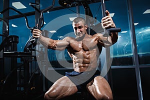 Athlete muscular bodybuilder training chest on simulator in the gym