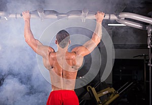 Athlete muscular fitness male model pulling up on horizontal bar in a gym.