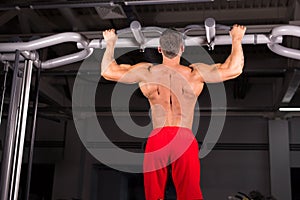 Athlete muscular fitness male model pulling up on horizontal bar in a gym.