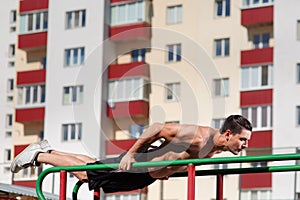 Athlete muscular fitness male model pulling up on horizontal bar on the outdoor.