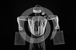 Athlete muscular man wear santa hat and apron. I have gift for you. Macho muscular torso posing with shopping bags