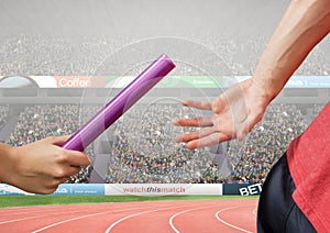 Athlete passing baton during relay race against stadium in background