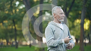 Athlete pensioner wiping sweat drinking water after outside training, fitness