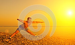 Athlete practicing, yoga on beach at suns