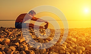 Athlete practicing, yoga on the beach at sunset