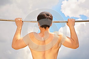 Athlete pull oneself up on sky background