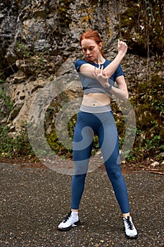 Athlete redhead female stretching body before jogging, running, outdoors alone