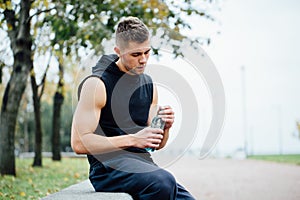 Athlete resting on bench in park after running with bottle of water. Rest a hard workout.