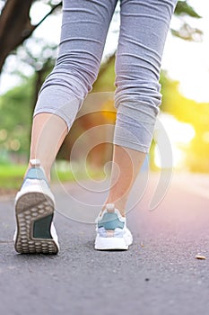 Athlete runner feet woman running in green park along road at sunrise morning