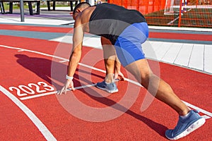 Athlete runner in a pose ready to start on a red treadmill line with the inscription numbers 2023. The concept of the beginning of