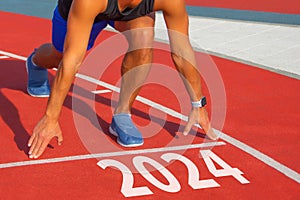 Athlete runner in a pose ready to start on a red treadmill line with the inscription numbers 2024. The concept of the beginning of