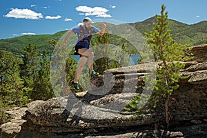 The athlete runs on the rocks in the mountains. Outdoor trail running in sunny day