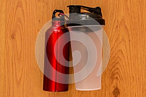 Athlete`s bottle of water and a red thermocafe on wooden background