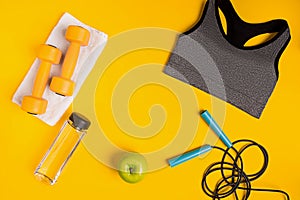 Athlete`s set with female clothing, dumbbells and bottle of water on yellow background