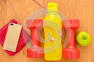Athlete`s set with two pink dumbbells, smarphone with pink headphones, green appple and a yellow bottle of water, in a