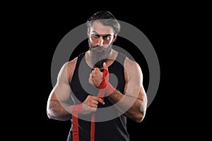 Athlete stands in black clothes and wraps his hands in red textile elastic bandage before training