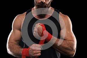 Athlete stands in black clothes and wraps his hands in red textile elastic bandage before training