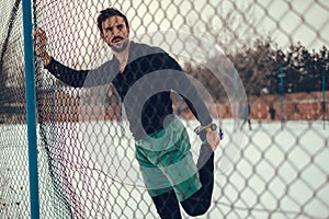 Athlete stretching quadriceps on the fence on a snowy day