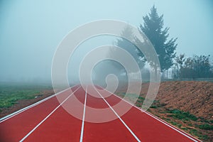 Atletická dráha nebo běžecká dráha v podzimní přírodě. Modré zamlžené pozadí. Bílá editační mezera