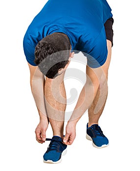 Athlete tying his shoelaces isolated over white background. Sportsman wearing black and blue sportswear ties his sneakers. Fitness