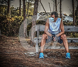 Athlete with virus protection mask resting on a wooden bench