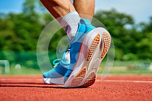 Athlete Wearing Bright Blue Running Shoes on Red Stadium Track During Training