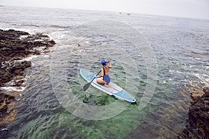 athlete woman in a blue swimsuit and bandana on stand up paddle board on a quiet blue ocean. Sup surfing in water