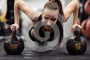 Athlete woman doing push ups on two kettlebells