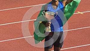 Athlete wrapped in his country flag victoriously holding deserved cup, triumph