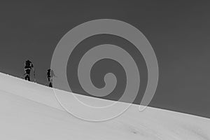 Athletes doing backcountry ski with a landscape of snowy mountains on a sunny day. Black and white