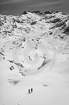 Athletes doing backcountry ski with a landscape of snowy mountains on a sunny day. Black and white