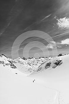 Athletes doing backcountry ski with a landscape of snowy mountains on a sunny day. Black and white