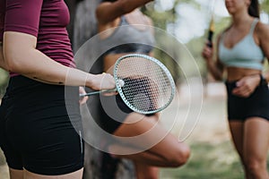 Athletes resting after training outdoors, holding rackets and a ball. Happy girls enjoying a conversation in a park on a