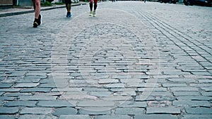 Athletes run along the paved stone road, city marathon, runners` legs close-up, sports competition