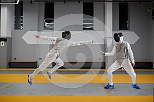 Athletes in uniforms and protective helmet mask fighting duel with rapiers
