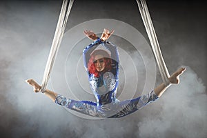 Athletic aerial circus artist with redhead in blue costume dancing in the air with balance