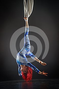 Athletic aerial circus artist with redhead in blue costume making tricks on the aerial silk