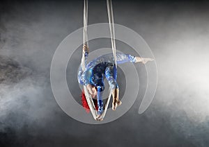 Athletic aerial circus artist with redhead in blue costume standing on one hand in the aerial silk