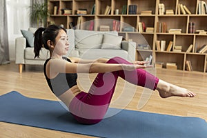 Athletic asian lady doing yoga, performing boat pose during her domestic workout on yoga mat at home
