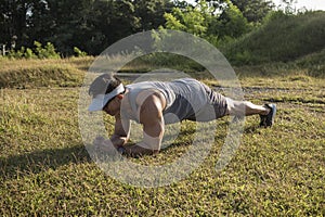 An athletic asian man does planks on the grass at a open field outdoors. Core and abdominal bodyweight exercise or calisthenics